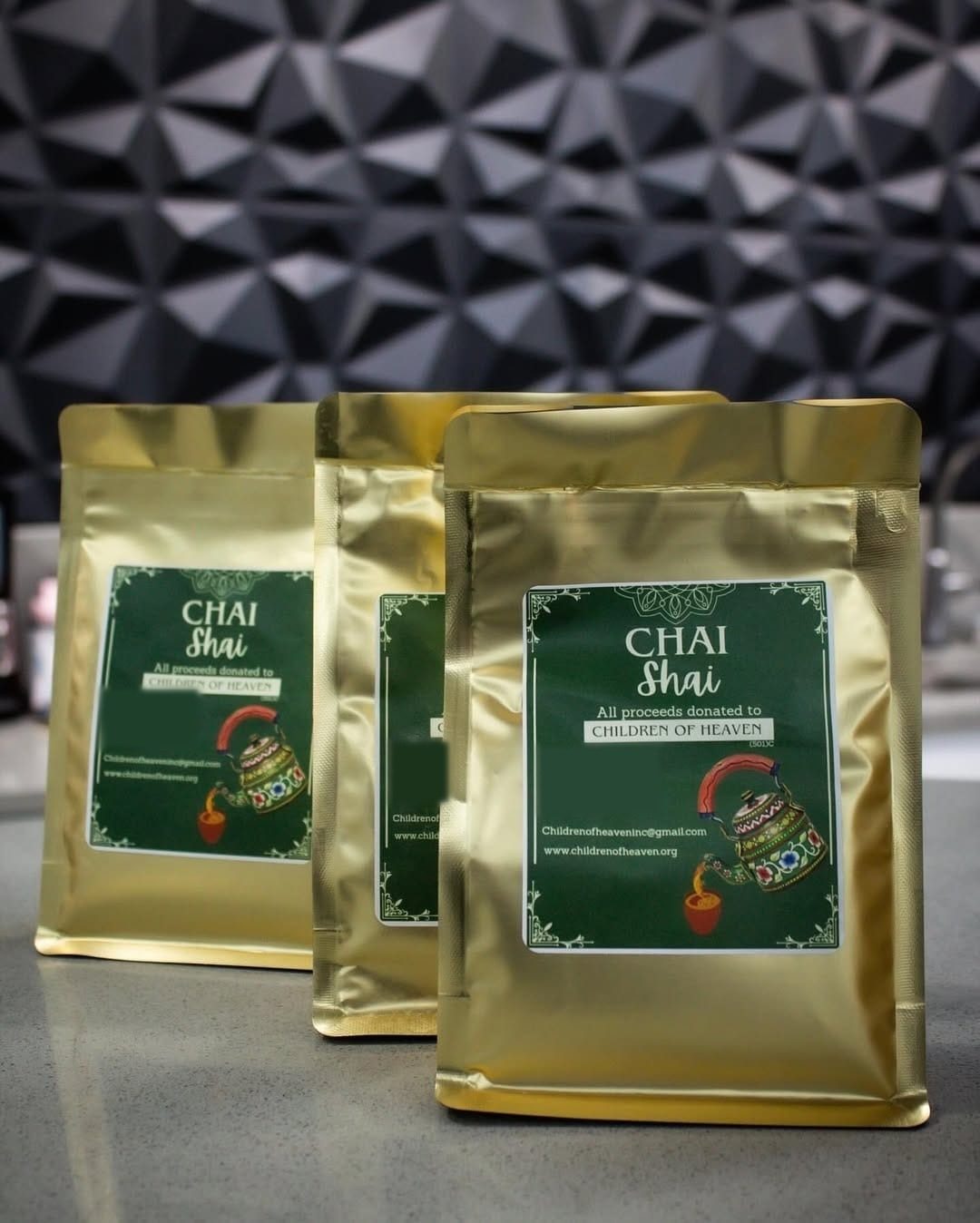 Three gold pouches of Chai Shaii Mehfil with deep green labels, against a dark geometric wall
